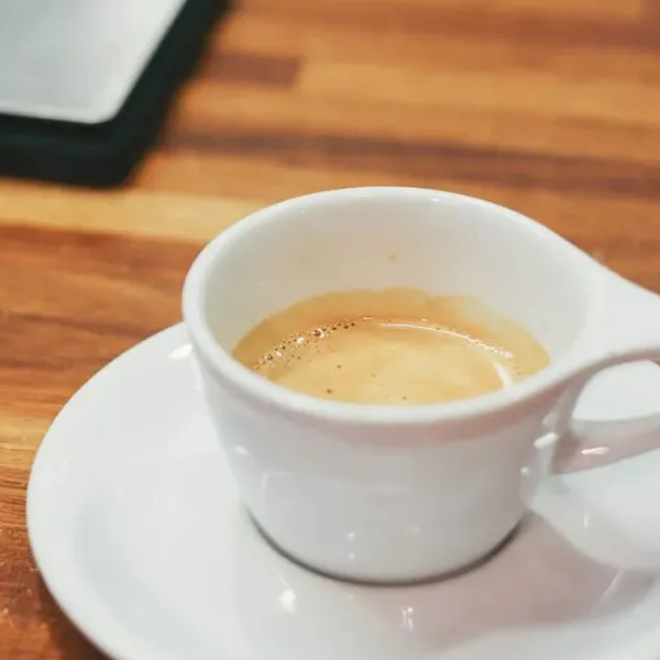 White espresso cup with crema on a saucer over a wooden countertop