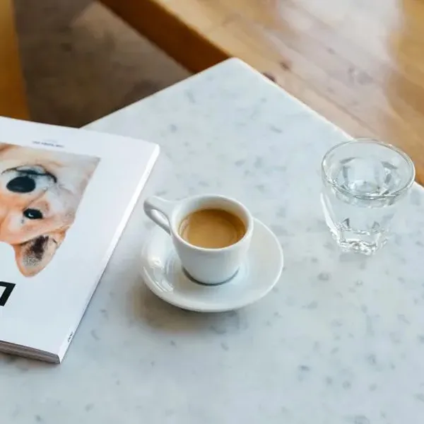 Cup of espresso on a marble table next to a glass of water and a magazine