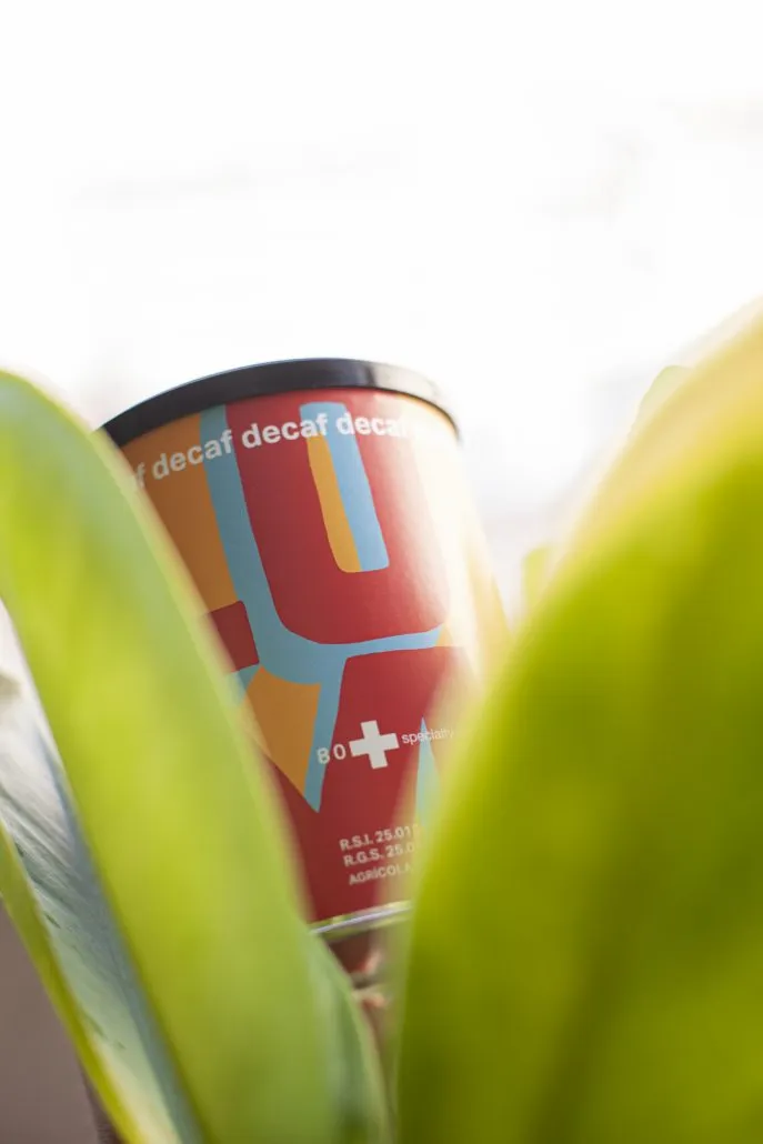 80plus decaffeinated specialty coffee packaging surrounded by green leaves