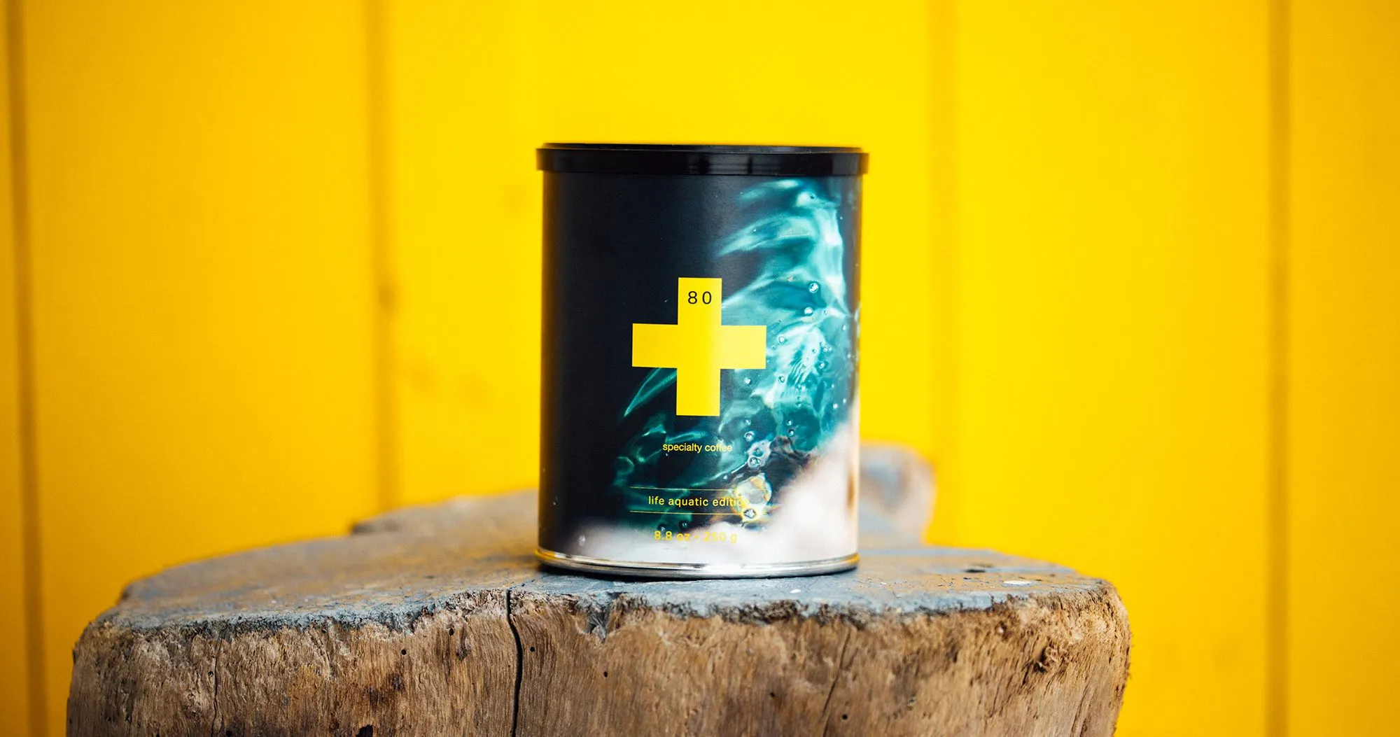 250g tin of 80plus specialty coffee on a wooden surface against a yellow background