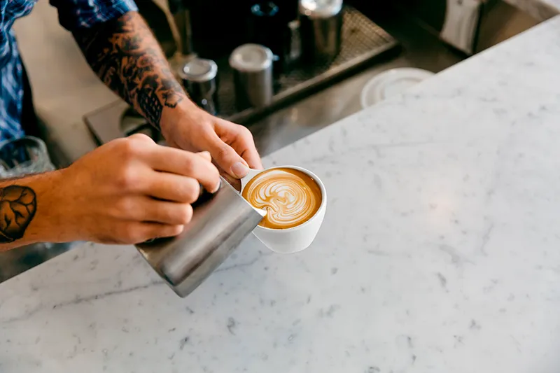 Barista pouring milk into a white cappuccino cup to create latte art